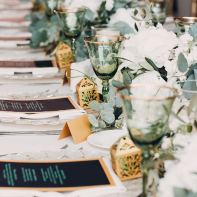 Table dressée avec des verres verts, fleurs blanches et menus décoratifs.