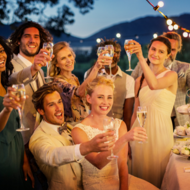 Groupe de mariage levant des verres en célébration, avec décor festif en plein air.