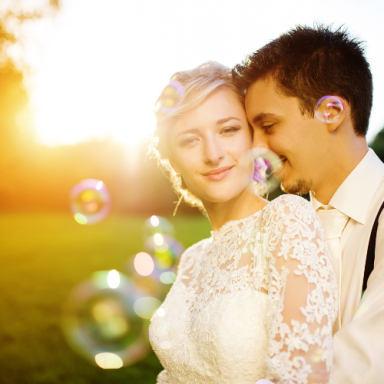 Un couple de mariés souriant avec des bulles et un coucher de soleil en arrière-plan.