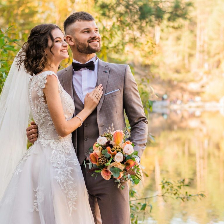 Un couple de mariés posant devant un lac, entouré d'une nature automnale.