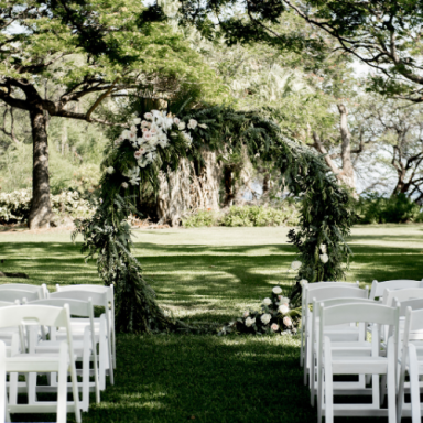 Arche de fleurs verdoyantes au milieu d'un espace extérieur avec chaises blanches.