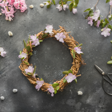 Couronne en brindilles ornée de fleurs, sur fond gris avec quelques pierres.
