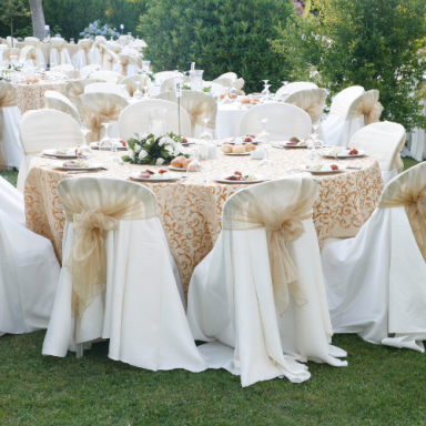 Tables élégamment dressées avec nappes dorées et chaises ornées de rubans en tulle.