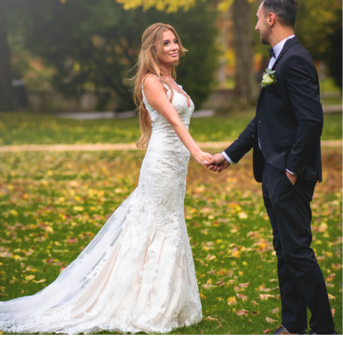 Un couple se tenant par la main dans un parc, vêtus d'une robe de mariée et d'un costume.