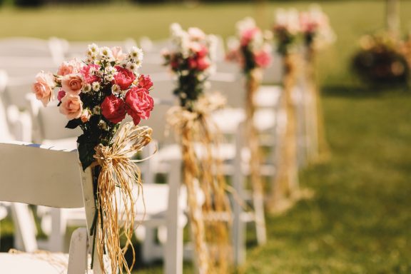Chaises blanches décorées de fleurs roses et rouges, avec de la jute, pour une cérémonie extérieure.