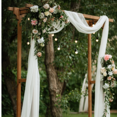 Arcade en bois décorée de fleurs et drapée de tissu, avec guirlandes lumineuses.